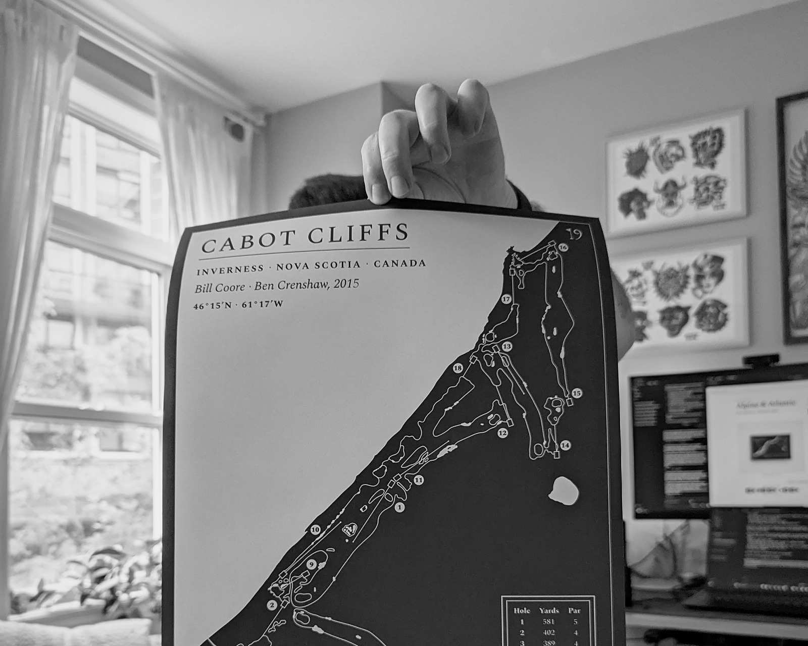 A hand-drawn Cabot Cliffs print held up in front of a wall of tattoo flash.
